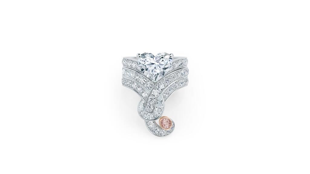 A crown ring featuring a 3.20-carat heart-shaped diamond with pavé-set diamonds and channel-set step-cut diamonds, and a 0.15-carat fancy pink oval-shaped diamond set in rose gold that sits at the tip of the ring De Beers high jewelry Tenderness Crown Ring